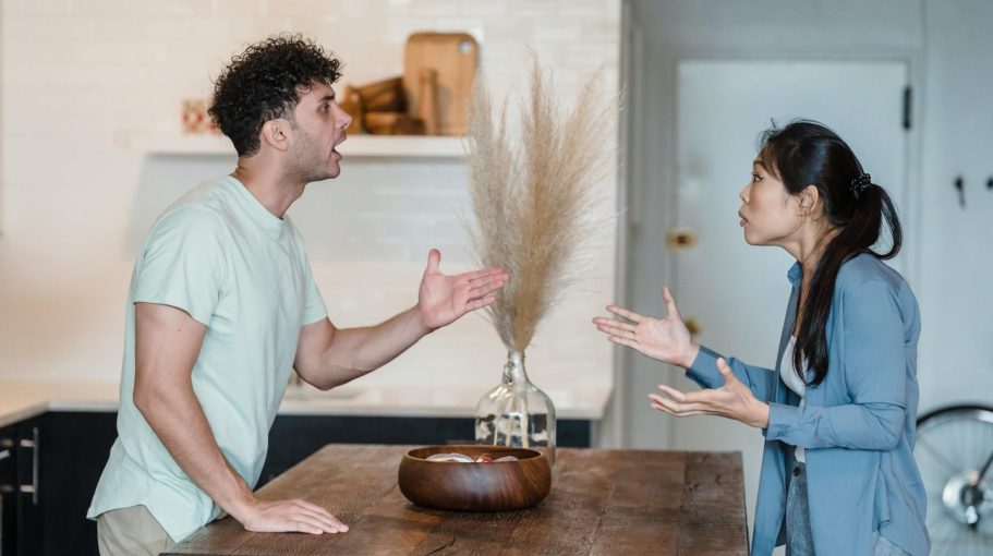 Two people engaged in a heated argument at a kitchen table.